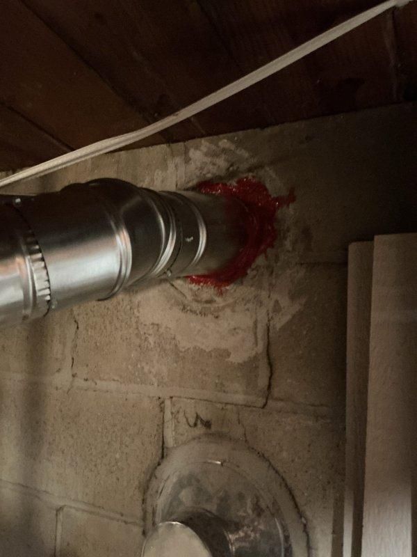 Installed new metal chimney liner through concrete block wall in basement utility area. Applied red fire-stopping sealant at wall penetration point to ensure proper sealing and fire code compliance. Connected and secured parallel galvanized ductwork runs with metal bands/clamps along ceiling area, completing the ventilation system installation.