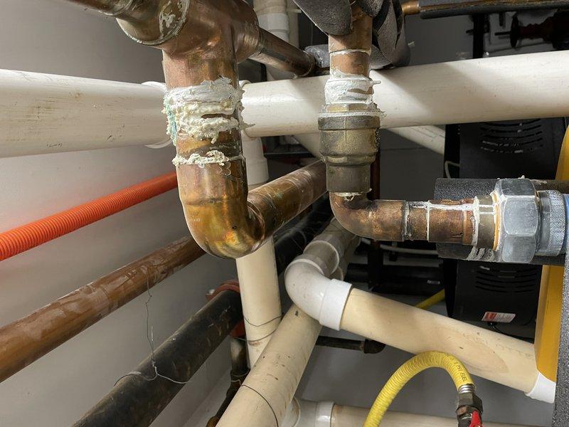 Inspected copper piping system identified by code enforcement for patina repair requirements. Evaluated extensive oxidation and corrosion on copper pipe fittings and joints, particularly at elbow connections. Documented condition of the plumbing network including affected copper components, PVC sections, and associated insulated lines for remediation planning.