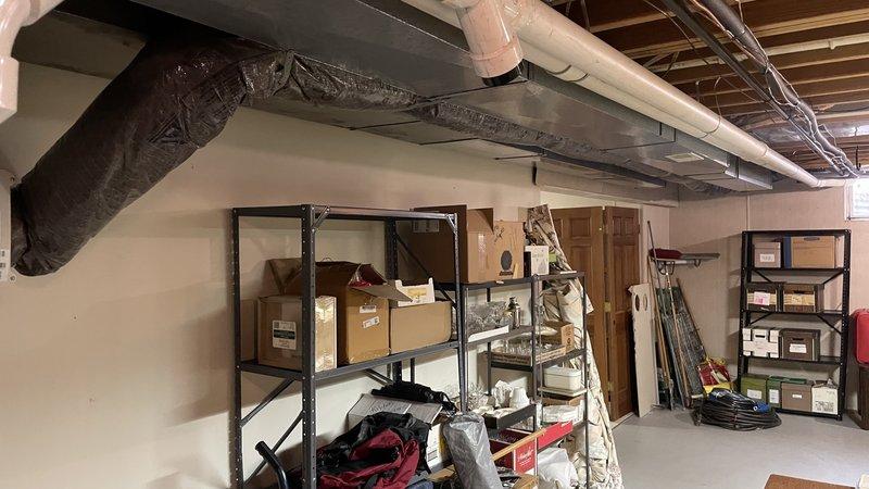 Completed ductwork renovation in unfinished basement utility area. Installed new insulated black duct through ceiling joists and added silver foil insulated ductwork with diamond pattern texture in adjacent area. Ensured proper sealing at wall junctions and verified all connections were secure for optimal HVAC system performance.
