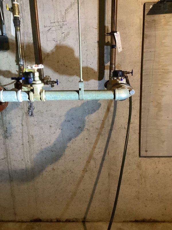 Inspected main water supply valve to sprinkler system located in basement utility area. Identified 1½-inch brass gate valve with blue handle connected to PVC piping system. Confirmed functionality of pressure regulator valve and verified proper operation of the shutoff mechanism as requested by sprinkler company.