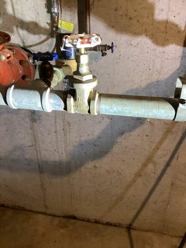 Inspected main water supply valve to sprinkler system located in basement utility area. Identified 1½-inch brass gate valve with blue handle connected to PVC piping system. Confirmed functionality of pressure regulator valve and verified proper operation of the shutoff mechanism as requested by sprinkler company.