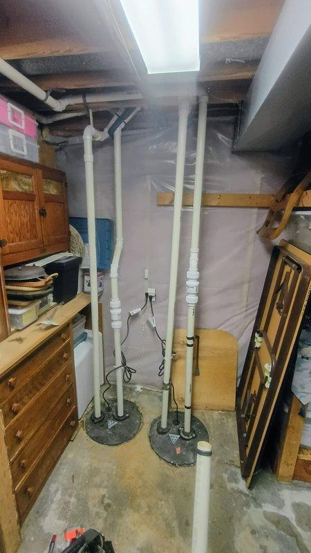Installed sump pump in basement utility area, connecting to existing PVC drain system with appropriate fittings and joints. Configured horizontal and vertical pipe sections to ensure proper water flow, addressing moisture issues evident on concrete floor.