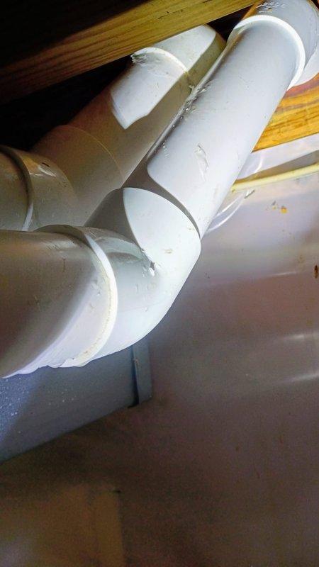 Installed sump pump in basement utility area, connecting to existing PVC drain system with appropriate fittings and joints. Configured horizontal and vertical pipe sections to ensure proper water flow, addressing moisture issues evident on concrete floor.
