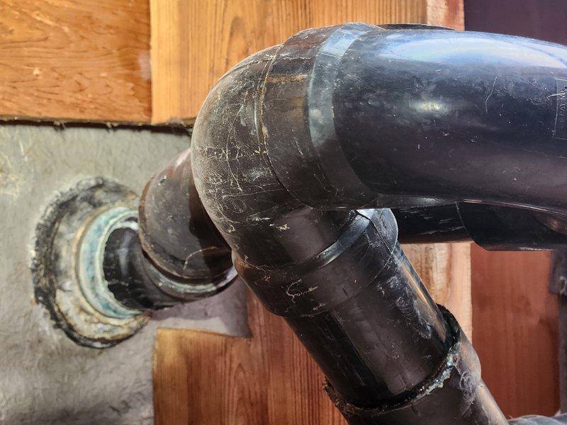 Responded to a plumbing emergency where a broken shower floor drain was causing water to leak into the basement. Upon inspection, identified failed drain assembly and deteriorated piping connections in the crawl space above the basement. Accessed the affected area through the attic/crawl space and examined the galvanized steel supply lines and black ABS drain piping system. The metal drain flange penetrating through the foundation wall showed significant corrosion and compromised seals at the connection points. Assessed the entire drainage configuration, including the elbow joints and horizontal drain runs, to determine the extent of the failure. Documented the condition of the existing plumbing infrastructure, including the aged drain fittings and deteriorated coupling connections between the metal flange and plastic piping system.