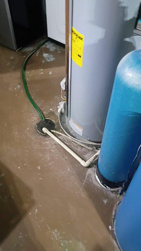 Conducted on-site assessment of existing water softener system in basement mechanical room, which is over 20 years old and requires replacement. Documented current plumbing configuration including blue cylindrical water softener tank, well pressure tank, water heater, and associated PVC piping infrastructure. Noted significant water damage and flooding throughout basement utility area, with standing water covering concrete floor surface. Photographed existing equipment layout and plumbing connections to prepare comprehensive replacement estimate for new water softener installation, including necessary modifications to accommodate updated system and address water intrusion issues.