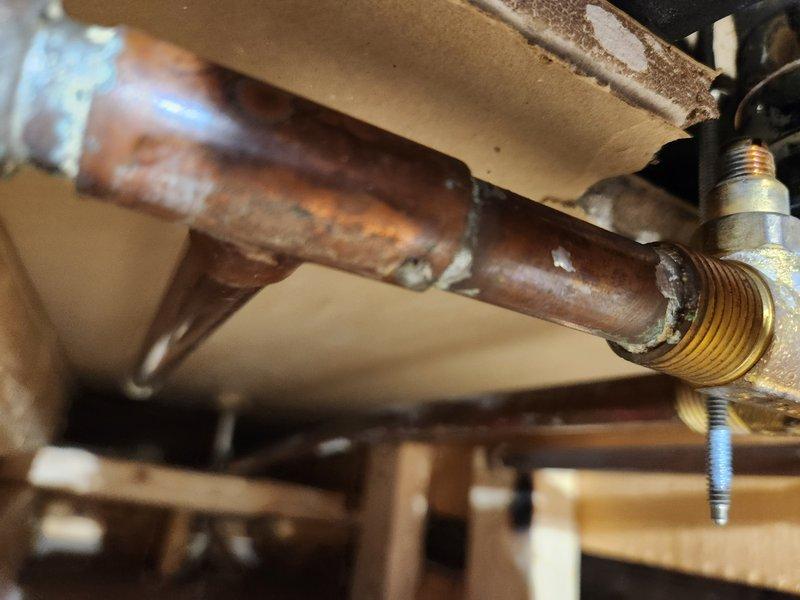 Responded to service call for burst pipe caused by freezing conditions. Upon arrival, confirmed water supply was shut off and pipe was no longer actively leaking. Conducted thorough inspection of plumbing infrastructure in crawlspace area beneath flooring. 

Identified heavily corroded horizontal steel pipe with significant rust deterioration throughout visible sections. Corrosion had compromised pipe integrity, contributing to failure when subjected to freezing temperatures. Pipe exhibited reddish-brown patina consistent with advanced oxidation. Adjacent brass threaded fittings showed minimal corrosion compared to main pipe section.

Documented existing plumbing configuration consisting of blue PEX cold water line and orange PEX hot water line running parallel beneath floor joists. Lines were properly secured with black plastic mounting brackets. Copper elbow fittings showed age-appropriate oxidation. Assessed structural mounting points and verified adequate support for existing and r
