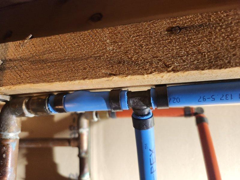 Responded to service call for burst pipe caused by freezing conditions. Upon arrival, confirmed water supply was shut off and pipe was no longer actively leaking. Conducted thorough inspection of plumbing infrastructure in crawlspace area beneath flooring. 

Identified heavily corroded horizontal steel pipe with significant rust deterioration throughout visible sections. Corrosion had compromised pipe integrity, contributing to failure when subjected to freezing temperatures. Pipe exhibited reddish-brown patina consistent with advanced oxidation. Adjacent brass threaded fittings showed minimal corrosion compared to main pipe section.

Documented existing plumbing configuration consisting of blue PEX cold water line and orange PEX hot water line running parallel beneath floor joists. Lines were properly secured with black plastic mounting brackets. Copper elbow fittings showed age-appropriate oxidation. Assessed structural mounting points and verified adequate support for existing and r