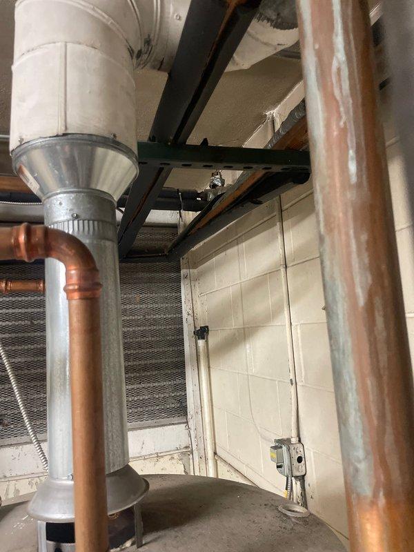 # HVAC System Assessment and Replacement Estimate

Conducted comprehensive on-site evaluation of existing residential boiler heating system and domestic water heating equipment located in basement mechanical room. Current system consists of Lochinvar water heater and aging boiler unit with associated copper supply lines, gas piping infrastructure, and exhaust venting. 

Documented existing installation including:
- Lochinvar brand water heater with multiple copper connections and control valves
- Gray boiler/heating unit with metal exhaust vent system
- Yellow gas supply piping routed along ceiling joists
- Copper water lines with red and blue handled shut-off valves
- Galvanized ductwork connections and white flexible duct runs
- Concrete block foundation walls and exposed ceiling joists
- Electrical connections and floor-mounted equipment positioning

Performed visual inspection of all mechanical components to assess current system condition, configuration, and replacement requiremen