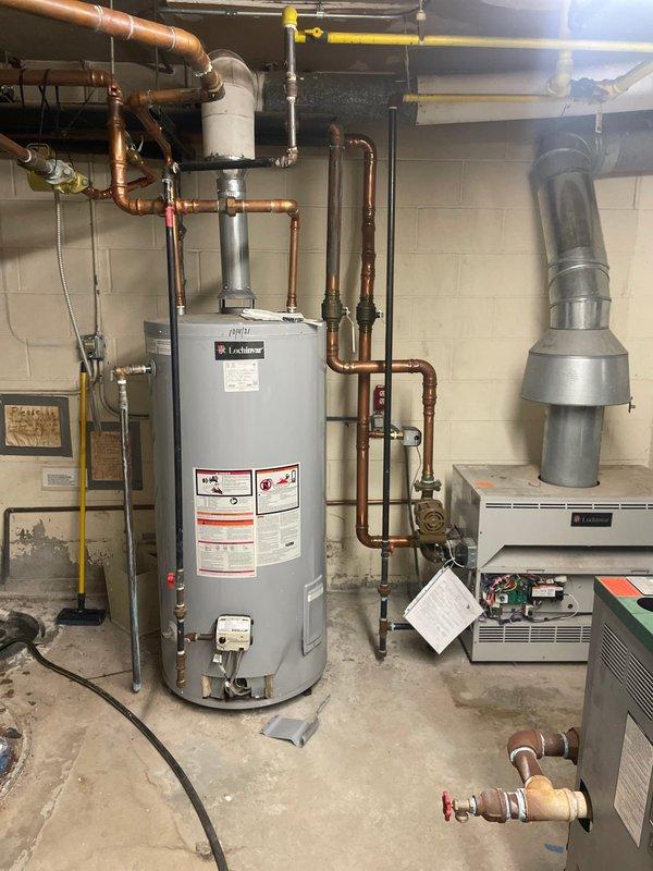 # HVAC System Assessment and Replacement Estimate

Conducted comprehensive on-site evaluation of existing residential boiler heating system and domestic water heating equipment located in basement mechanical room. Current system consists of Lochinvar water heater and aging boiler unit with associated copper supply lines, gas piping infrastructure, and exhaust venting. 

Documented existing installation including:
- Lochinvar brand water heater with multiple copper connections and control valves
- Gray boiler/heating unit with metal exhaust vent system
- Yellow gas supply piping routed along ceiling joists
- Copper water lines with red and blue handled shut-off valves
- Galvanized ductwork connections and white flexible duct runs
- Concrete block foundation walls and exposed ceiling joists
- Electrical connections and floor-mounted equipment positioning

Performed visual inspection of all mechanical components to assess current system condition, configuration, and replacement requiremen