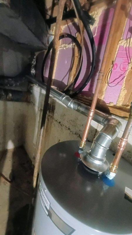 Replaced existing tanked water heater with new unit in basement utility area. Removed old dark gray/black water heater and installed new white residential water heater. Connected copper supply lines, pressure relief valve assembly, and flexible connectors to top of new tank. Completed all plumbing connections and electrical wiring per manufacturer specifications. Unit left unfilled with water per customer request pending further instructions. Installation positioned adjacent to existing blue water treatment system with all connections properly secured and accessible for future service.