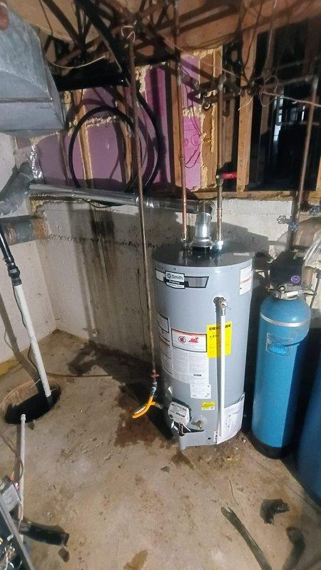 Replaced existing tanked water heater with new unit in basement utility area. Removed old dark gray/black water heater and installed new white residential water heater. Connected copper supply lines, pressure relief valve assembly, and flexible connectors to top of new tank. Completed all plumbing connections and electrical wiring per manufacturer specifications. Unit left unfilled with water per customer request pending further instructions. Installation positioned adjacent to existing blue water treatment system with all connections properly secured and accessible for future service.