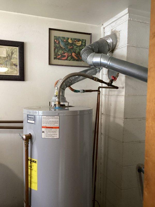 Completed water heater installation in residential basement utility area. Installed tanked water heater unit with proper copper supply line connections, flex connectors, and metallic venting system secured to wall with appropriate mounting brackets, ensuring all components meet code requirements for safe operation.