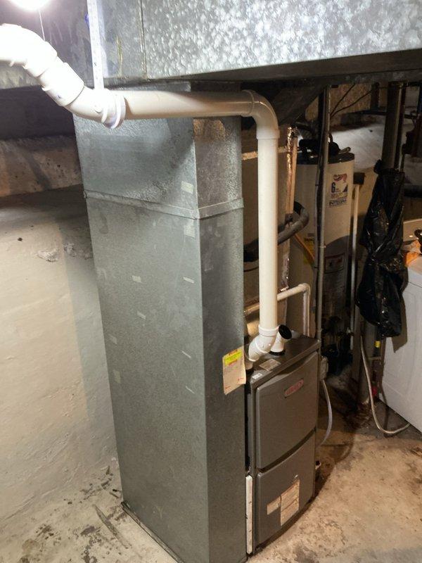 Completed installation of Lennox ML196UH045XE36BK high-efficiency furnace in basement mechanical room, including new condensate pump with tubing routed through white PVC piping system. Reconnected unit to existing return air drop and filter rack, installed new T4 thermostat for system control, and replaced air filter to ensure optimal airflow and system performance.