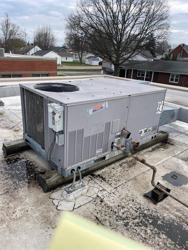 Conducted site walk-through of commercial property to assess HVAC equipment for maintenance plan development. Documented approximately 12 rooftop packaged air conditioning units showing varying degrees of age and weathering, with visible surface wear and discoloration on metal casings. Noted deteriorated roofing conditions around unit bases including cracked concrete, damaged membrane material, and rust staining across white roofing surface requiring attention during future maintenance visits.