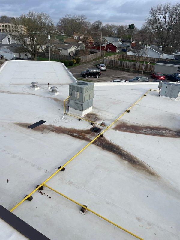 Conducted site walk-through of commercial property to assess HVAC equipment for maintenance plan development. Documented approximately 12 rooftop packaged air conditioning units showing varying degrees of age and weathering, with visible surface wear and discoloration on metal casings. Noted deteriorated roofing conditions around unit bases including cracked concrete, damaged membrane material, and rust staining across white roofing surface requiring attention during future maintenance visits.