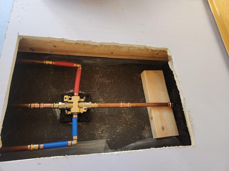 Installed new Delta shower and tub valve assembly with trim kit in existing bathtub enclosure. Accessed plumbing infrastructure through wall opening to connect supply lines to valve body using copper piping with brass compression fittings and PEX connections for hot and cold water supply. Mounted chrome shower fixture and faucet assembly on tiled wall surface and completed installation with proper trim kit components.