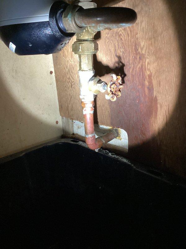 # Water Meter Leak Repair

Responded to a water leak at the meter assembly leaking approximately 2 gallons per hour. Upon arrival, water was not shut off and no standing water was present on site. Inspection revealed significant corrosion and mineral buildup on brass fittings at the meter connection point, with white and blue-green deposits indicating long-term deterioration. The leak originated from corroded threads on the brass shutoff valve assembly where it connects to the copper supply line.

Documented existing conditions showing advanced corrosion on metallic fittings, aged copper piping with patina, and mineral scaling around connection points. The plumbing assembly was mounted against a wooden backing in what appears to be a utility or basement area. A condensate pump with copper piping connections was also present in the service area, with a drip pan positioned beneath for leak protection.

Confirmed with municipality that repair responsibility falls to the homeowner. Provide