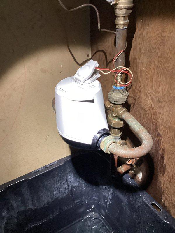 # Water Meter Leak Repair

Responded to a water leak at the meter assembly leaking approximately 2 gallons per hour. Upon arrival, water was not shut off and no standing water was present on site. Inspection revealed significant corrosion and mineral buildup on brass fittings at the meter connection point, with white and blue-green deposits indicating long-term deterioration. The leak originated from corroded threads on the brass shutoff valve assembly where it connects to the copper supply line.

Documented existing conditions showing advanced corrosion on metallic fittings, aged copper piping with patina, and mineral scaling around connection points. The plumbing assembly was mounted against a wooden backing in what appears to be a utility or basement area. A condensate pump with copper piping connections was also present in the service area, with a drip pan positioned beneath for leak protection.

Confirmed with municipality that repair responsibility falls to the homeowner. Provide