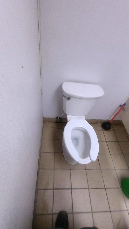 Responded to service call for toilet requiring reseating in main office restroom. Upon arrival, assessed the toilet installation and identified improper seal between the fixture and floor flange. Removed existing toilet by disconnecting water supply line, unbolting mounting hardware, and lifting unit from floor flange. Scraped and cleaned old wax ring residue from both the toilet base and closet flange to ensure proper seal. Inspected flange for damage and verified structural integrity before proceeding. Installed new wax ring on flange, carefully repositioned toilet over mounting bolts, and compressed seal by applying even pressure. Secured toilet to floor with new mounting hardware, reconnected water supply line, and tested for leaks and proper operation. Verified stable installation with no rocking or movement, confirmed adequate flush performance, and left work area clean.