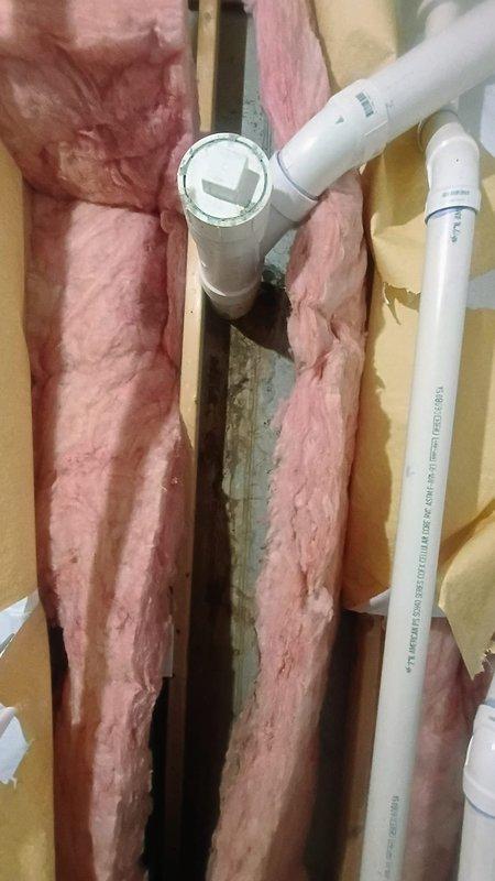 Responded to basement water leak complaint involving pipe penetration through foundation wall. Upon inspection, identified active leak at pipe seal where plumbing line passes through wall cavity between floor joists. Documented conditions showing PVC drainage pipe running vertically through wooden framing with visible moisture damage, discoloration, and staining on surrounding wood framing members and insulation materials. Evidence of water intrusion observed with brownish-gray staining and greenish-blue discoloration on backing materials and insulation, indicating ongoing moisture exposure. Photographed compromised pipe seal, damaged insulation, and affected structural components for assessment. Water supply remained active during initial inspection to verify leak source and extent of damage.