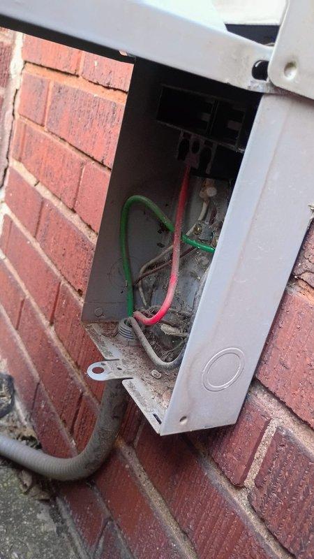 Responded to service call for stolen AC connections. Upon arrival, found electrical disconnect box mounted on exterior brick wall with cover open and copper conductors removed from unit. Documented existing conditions showing remaining ground wire, partial wiring, and conduit entry point. Advised customer of necessary repairs including replacement of stolen copper wiring and reconnection of HVAC system electrical supply.