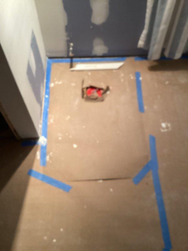Completed plumbing inspection for shower drain gurgling issue that occurs when main floor toilet is flushed, indicating potential drainage or venting concern. Documented existing shower pan installation showing two drain assemblies with visible staining and deterioration along perimeter edges where pan meets walls. Protective flooring materials in place suggest ongoing renovation work; photographed conditions for insurance estimate documentation related to previously discussed work requiring concrete removal equipment.