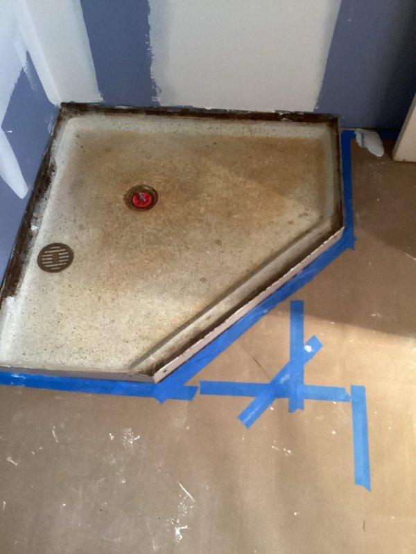 Completed plumbing inspection for shower drain gurgling issue that occurs when main floor toilet is flushed, indicating potential drainage or venting concern. Documented existing shower pan installation showing two drain assemblies with visible staining and deterioration along perimeter edges where pan meets walls. Protective flooring materials in place suggest ongoing renovation work; photographed conditions for insurance estimate documentation related to previously discussed work requiring concrete removal equipment.