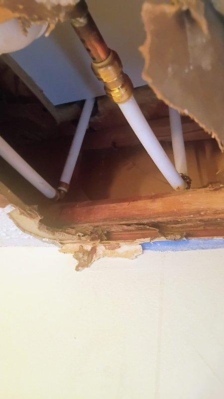 Responded to upstairs bathroom shower leak affecting first floor ceiling. Upon arrival, water supply was already shut off with no standing water present. Accessed ceiling cavity below upstairs bathroom to locate source of leak. Inspection revealed active leak at PVC drain piping connection point serving shower fixture. Observed water damage and staining on wooden framing members and ceiling joists from prolonged moisture exposure. Identified compromised brass compression fitting on white PVC drain line as primary leak source. Documented existing conditions including damaged drywall, exposed plumbing infrastructure, and deteriorated ceiling materials. Assessed structural impact to wooden framing and extent of water infiltration into first floor ceiling space.