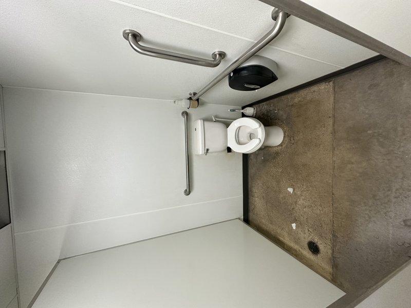 Returned to site to conduct detailed assessment and documentation of accessible restroom facilities for quoting purposes. Photographed existing toilet installation, ADA-compliant grab bar configuration, wall-mounted fixtures, and plumbing infrastructure including visible PVC drainage components. Documented current conditions of white partition walls, stainless steel safety rails, and dispenser mounting locations to provide accurate scope of work for upcoming service requirements.