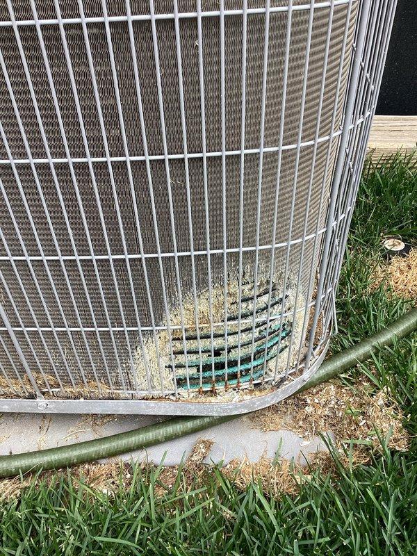 Performed comprehensive cooling system tune-up on residential air conditioning unit. System was found operating properly with no functional issues reported. Exterior inspection revealed moderate accumulation of debris, dirt, and organic material around base and wire guard assembly, which was documented photographically. Cleaned condenser coils, removed debris buildup from unit perimeter, and verified proper airflow through fan assembly. Inspected refrigerant lines, electrical connections, and mounting pad for integrity. All components tested within normal operating parameters with no immediate concerns identified regarding long-term system performance.