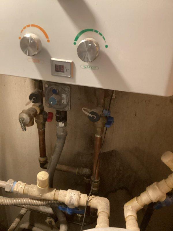 Responded to vacant rental property for water leak assessment under slab foundation. Confirmed water supply was shut off with no standing water present. Inspected water heater connections and exposed plumbing infrastructure, documenting copper pipe conditions, PVC routing, and valve configurations. Evaluated existing plumbing layout including wall-mounted water heater with visible control panel, brass fittings, and distribution lines. Photographed plumbing system within wall cavity showing white control unit, PVC piping, flexible tubing connections, and wooden framing structure. Provided findings via phone and email per property owner's request, including documentation of current system conditions and recommendations for re-routing options to bypass under-slab leak location as preferred repair method.