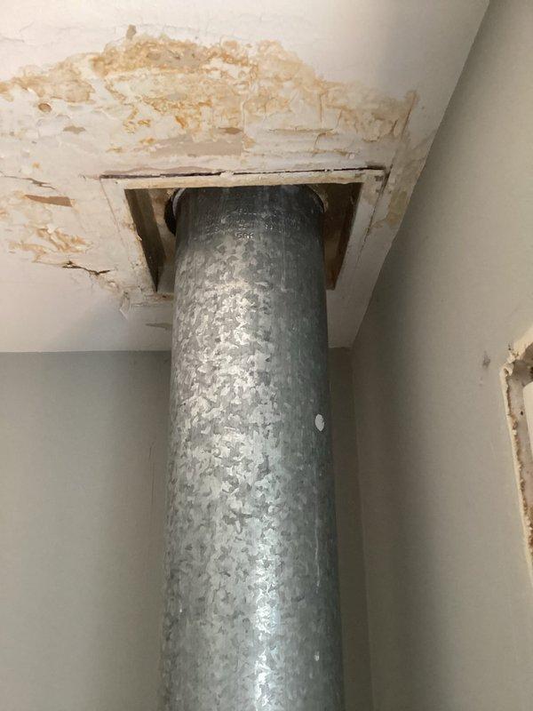 Responded to service call for damaged vent pipe penetrating roof assembly causing water intrusion in 1984-constructed residence. Upon inspection, identified compromised galvanized metal vent stack extending from basement through roof with visible split/hole allowing moisture infiltration around pipe penetration point. Found extensive ceiling damage surrounding duct opening, including deteriorated drywall, peeling paint, and compromised substrate material from prolonged water exposure. Temporary tape repair was in place from previous attempt. Documented condition of vertical vent run showing surface condensation on insulated sections and assessed structural damage to ceiling materials and wooden framing around penetration. Photographed damaged areas for repair documentation. Confirmed no immediate gas odor or safety hazards present at time of inspection.