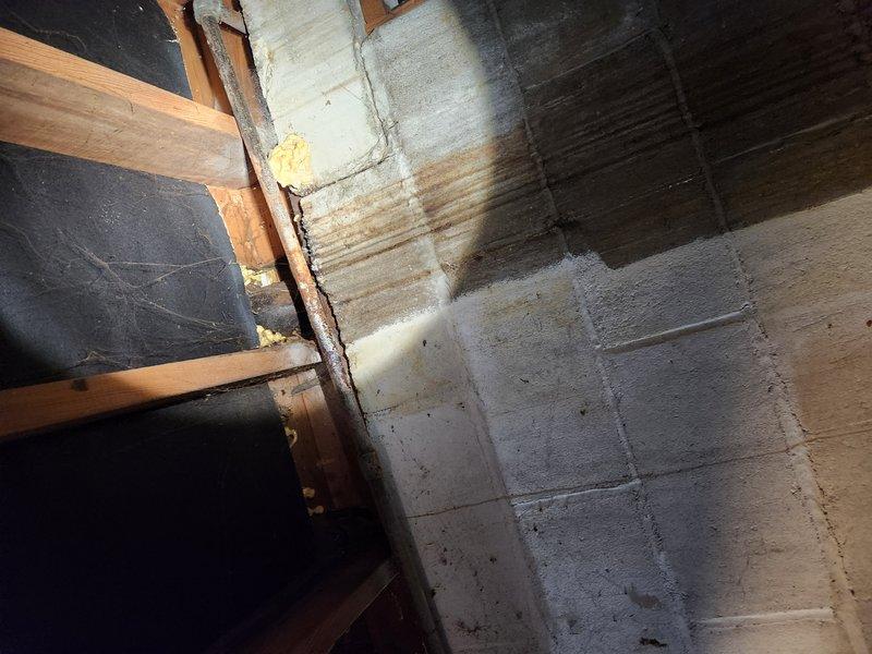 Responded to basement water leak call and coordinated access with tenant. Upon inspection, discovered severely corroded plumbing component in basement crawl space showing extensive rust damage from prolonged moisture exposure. The rusted spherical fixture exhibited heavy orange-brown corrosion throughout, with surrounding insulation material displaying significant deterioration and water damage. Assessed aging copper piping running along wooden floor joists near concrete block foundation wall with spray foam insulation. Documented conditions with photographic evidence showing compromised plumbing infrastructure and moisture-related degradation in confined basement space requiring repair recommendation.