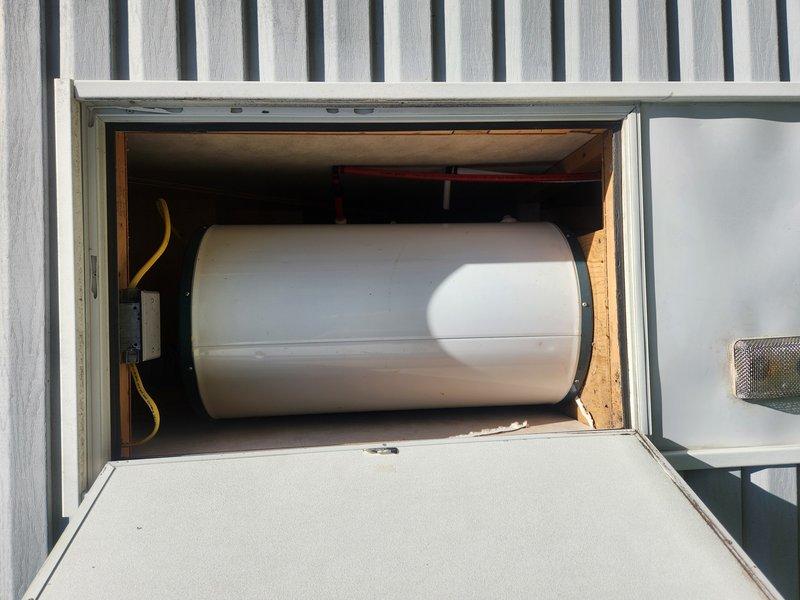 Responded to service call for non-operational tanked water heater less than five years old at campground facility. Upon arrival, accessed exterior storage compartment housing horizontally-mounted water heater unit secured with mounting straps. Performed diagnostic inspection of unit with no visible water leakage present. Accessed attic space to inspect related HVAC connections and verify proper venting and ductwork configuration. Documented equipment condition and compartment accessibility for repair recommendations.