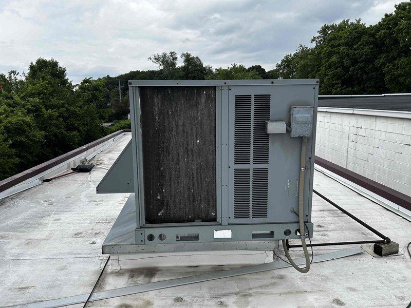 Conducted comprehensive site assessment of existing rooftop HVAC unit for replacement estimate. Unit exhibited significant weathering, discoloration, and streaking on access panels indicating prolonged environmental exposure and potential component degradation. Documented current equipment condition, mounting platform configuration, electrical connections, and conduit routing on flat membrane roof system. Evaluated installation parameters including roof accessibility, structural support requirements, and clearances for replacement unit specifications.