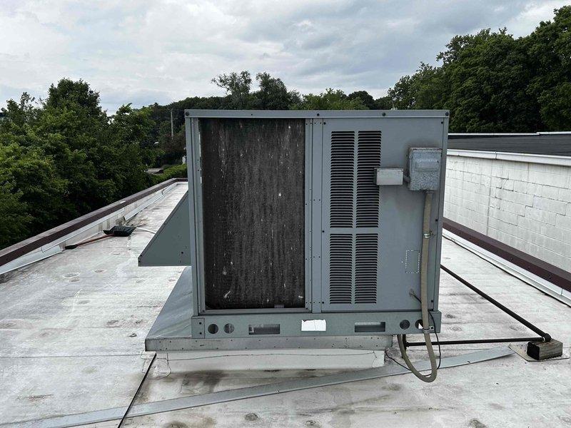 Conducted comprehensive site assessment of existing rooftop HVAC unit for replacement estimate. Unit exhibited significant weathering, discoloration, and streaking on access panels indicating prolonged environmental exposure and potential component degradation. Documented current equipment condition, mounting platform configuration, electrical connections, and conduit routing on flat membrane roof system. Evaluated installation parameters including roof accessibility, structural support requirements, and clearances for replacement unit specifications.