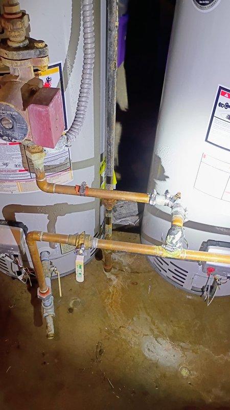 Responded to water leak emergency in basement utility area involving dual water heater system. Upon arrival, found active leak on recirculating line between water heaters spraying water across floor. Water was draining into floor drain but main shutoff valve was inaccessible or inoperable, preventing immediate water isolation. Assessed copper piping configuration, pressure relief valves, and connection points throughout the hot water distribution system. Documented extensive water staining on concrete floor and condition of brass fittings, flexible connectors, and plumbing infrastructure. Identified source of leak at recirculation line connection point near water heater installation.