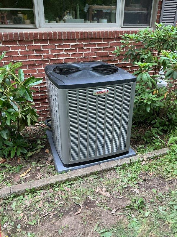 Completed installation of Lennox EL22XCV air conditioning system with S40 smart thermostat and equipment interface module at residential property. Unit was positioned on concrete pad against brick foundation with proper clearances maintained, electrical connections verified, refrigerant lines charged to manufacturer specifications, and system startup performed with temperature differential readings confirming optimal performance at 96.9°F discharge temperature.