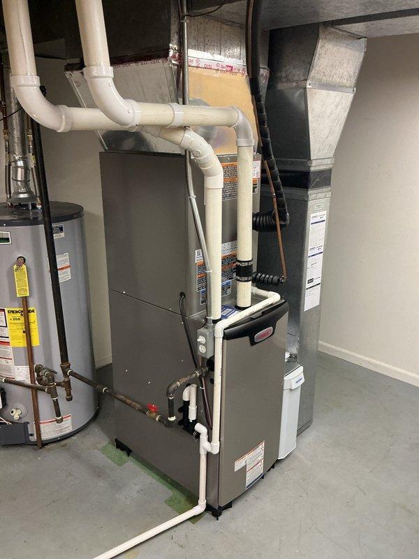 Completed full HVAC system installation including Lennox EL297UH070 high-efficiency furnace, ML17KC2-036 air conditioning unit, CK40CT-36B evaporator coil, 1410 filter cabinet, and S200 programmable thermostat. Installed furnace in basement utility area with proper PVC venting routed through overhead structure, connected refrigerant lines and condensate drainage using black flexible tubing, and completed all gas piping connections with brass fittings and shutoff valves. Mounted outdoor condensing unit on concrete pad against exterior wall with proper clearances, ran refrigerant linesets and electrical conduit through exterior wall penetration, installed white PVC condensate drain line along siding, and verified secure mounting of electrical disconnect box. Connected evaporator coil to furnace plenum, integrated filter cabinet into return air system, and completed all ductwork transitions to existing distribution system. Wired and programmed S200 thermostat for system operation, perform