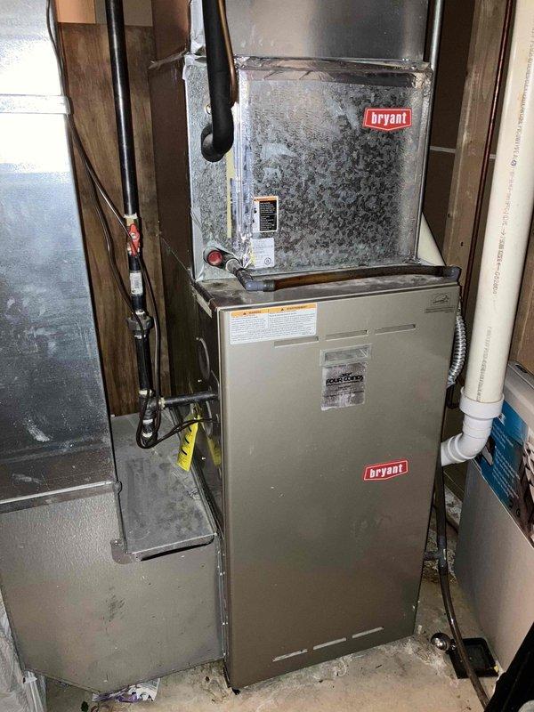 Conducted comprehensive HVAC system evaluation for complete replacement estimate at residential property. Assessed existing Bryant split system configuration consisting of outdoor condensing unit positioned on concrete pad with gravel drainage bed and indoor air handler/furnace combination located in basement mechanical room. Documented current equipment condition, noting significant condensation accumulation on evaporator coil unit indicating potential efficiency concerns, moisture staining at building foundation near outdoor unit suggesting drainage issues, and overall system age and performance characteristics. Evaluated electrical disconnect, refrigerant line routing, PVC condensate drainage, and existing ductwork connections to determine replacement specifications and compatibility requirements for new high-efficiency system installation.