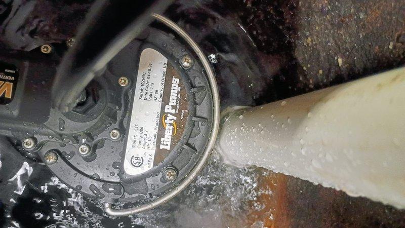 Responded to emergency call for malfunctioning sump pump in 1970s-era home basement. Upon arrival, assessed reported symptoms of unusual thumping noise and visible smoke emanating from pump unit prior to customer disconnecting power. Conducted visual inspection of sump pit area located near laundry facilities, noting moisture accumulation and pump assembly condition. Documented existing installation configuration including discharge piping, electrical connections, and pump housing with significant water exposure. Evaluated gray mechanical pump unit with multiple mounting bolts and observed wet concrete floor conditions around basin. Provided estimate for complete sump pump replacement to restore proper basement water removal functionality and prevent potential flooding issues.