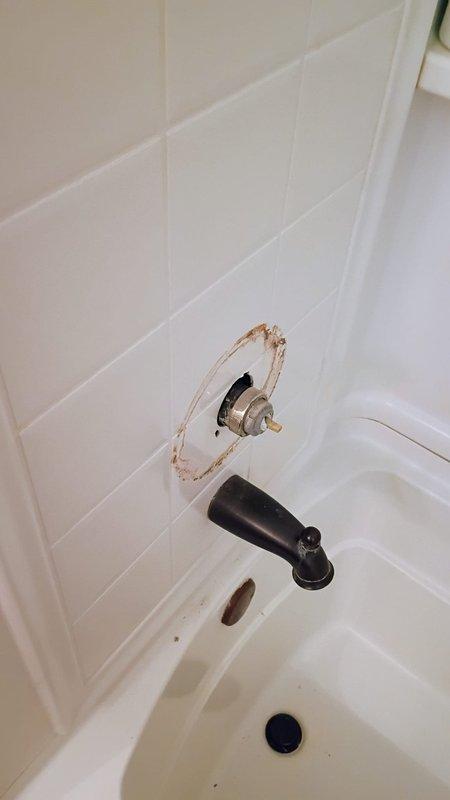 Responded to second-floor bathroom shower faucet installation issue involving a Delta 17 series valve assembly. Upon arrival, found significant wall damage around the existing faucet mounting area with deteriorated tile and exposed substrate creating an irregular 6-8 inch opening around the valve stem. Accessed plumbing through existing wall chase to assess copper supply line connections and valve positioning. Addressed installation complications preventing proper operation of the shower control valve's on/off mechanism. Documented existing conditions including compromised tile work and wall structure requiring remediation for proper faucet seating and water-tight installation.