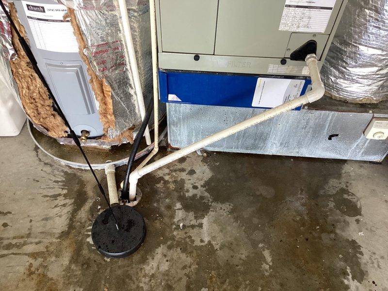 Responded to service call for water accumulation around furnace in garage area. Upon arrival, found extensive water pooling on concrete floor surrounding HVAC equipment and damaged reflective insulation on vertical ductwork with significant deterioration and peeling. Inspected 18-year-old heating system, condensate drain line, PVC piping, and galvanized drip pan for source of water leakage. Documented conditions showing moisture patterns throughout mechanical room area, damaged fiberglass insulation material, and water staining on floor surfaces. Evaluated condensate pump assembly, drain connections, and air handler unit with blue filter compartment to identify cause of water intrusion affecting garage space.