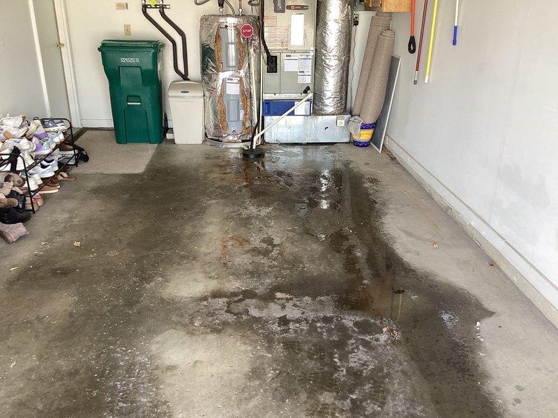 Responded to service call for water accumulation around furnace in garage area. Upon arrival, found extensive water pooling on concrete floor surrounding HVAC equipment and damaged reflective insulation on vertical ductwork with significant deterioration and peeling. Inspected 18-year-old heating system, condensate drain line, PVC piping, and galvanized drip pan for source of water leakage. Documented conditions showing moisture patterns throughout mechanical room area, damaged fiberglass insulation material, and water staining on floor surfaces. Evaluated condensate pump assembly, drain connections, and air handler unit with blue filter compartment to identify cause of water intrusion affecting garage space.