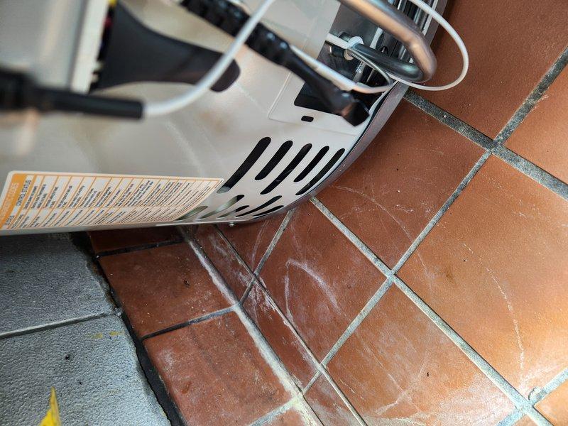 Responded to callback for water heater leak following recent installation. Upon inspection, identified active leak at expansion tank connection point where copper supply line joins the tank via brass push-fit fitting and silver adapter coupling. Evidence of water damage observed on terracotta tile flooring beneath the water heater unit, with visible moisture staining and discoloration on multiple tiles near the base of the appliance. Documented leak source and water damage with photographs showing the failed connection assembly and affected flooring area. The expansion tank mounting and flexible connector hose appeared intact, with leak isolated to the threaded adapter joint at the tank inlet. Recommended immediate repair of the faulty connection to prevent further water damage to the flooring and surrounding area.