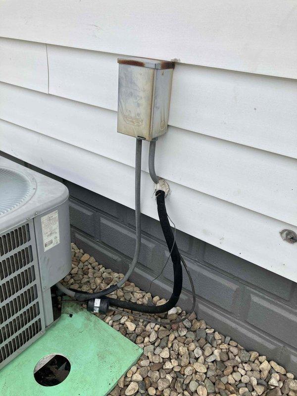 Performed comprehensive assessment of existing HVAC system for complete replacement estimate. Evaluated aging air conditioning unit over 10 years old that was non-operational, affecting entire residence. Inspected exterior condenser unit, electrical disconnect box showing significant weathering and rust deterioration, refrigerant line sets, condensate drainage system, and ductwork installation on exterior brick wall. Documented current system configuration including galvanized metal ductwork, electrical conduit routing, and equipment placement on gravel pad. Provided homeowner with quote options for both full HVAC system replacement and air conditioning unit replacement only.