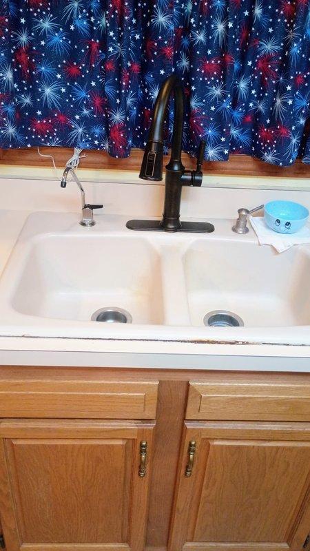 Returned to address ongoing leak at hot water supply line in bathroom that was previously serviced. Inspected hot water lead connection, identified source of continued leak, and performed necessary repairs to resolve the issue. Documented conditions with photographs of exterior plumbing penetration and interior kitchen plumbing fixtures for service records.