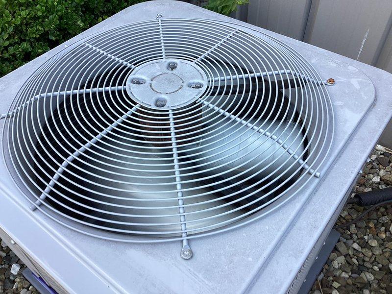 Responded to no cooling complaint on property with three 26-year-old HVAC systems all blowing warm air. Performed diagnostic inspection on outdoor condenser units, accessing electrical compartment to examine dual run capacitors, contactor assemblies, and associated wiring. Documented system conditions with photos showing condenser fan assembly, protective guard, and internal electrical components including capacitors mounted on platform with connecting wires and refrigerant lines.