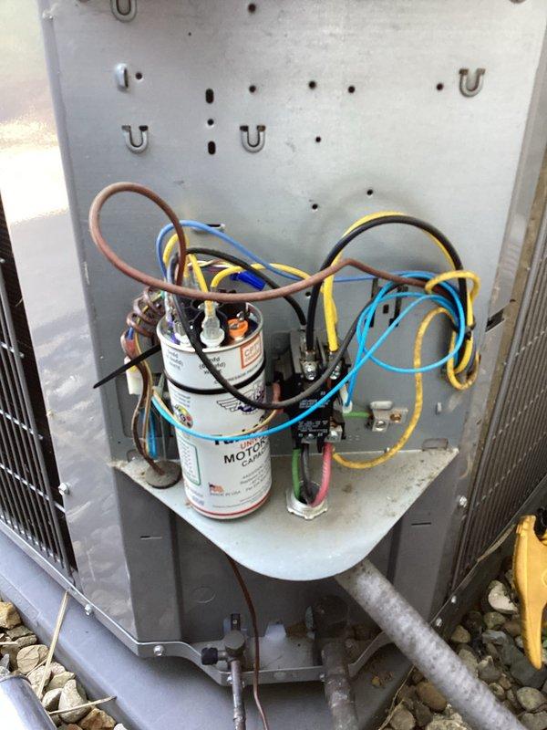 Responded to no cooling complaint on property with three 26-year-old HVAC systems all blowing warm air. Performed diagnostic inspection on outdoor condenser units, accessing electrical compartment to examine dual run capacitors, contactor assemblies, and associated wiring. Documented system conditions with photos showing condenser fan assembly, protective guard, and internal electrical components including capacitors mounted on platform with connecting wires and refrigerant lines.