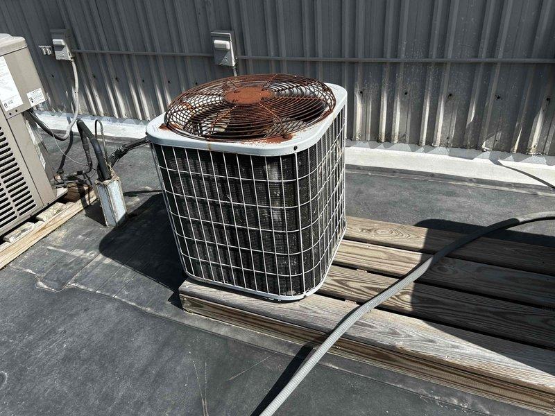 Conducted rooftop HVAC assessment for two barely-functioning air conditioning systems on commercial property. Evaluated multiple rooftop package units installed on elevated platform with rubber membrane roofing, documenting existing equipment conditions including cylindrical condenser unit with cage housing and rectangular rooftop AC units mounted on metal curbs. Photographed current system configurations, electrical disconnects, conduit routing, and mounting platforms to prepare comprehensive replacement estimate for dual AC system installation.